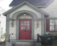 This photograph shows the elaborate entrance porch, the bracketed horse-shoe entablature and fanned wooden transom over the wood door with multi-paned glass panels, 2005; City of Saint John