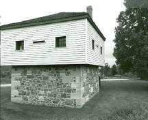 Corner view of the Blockhouse, showing the square, two-storey massing with pyramidal roof and chimney, 1989.; Department of Public Works / Ministère des Travaux publics, 1989.