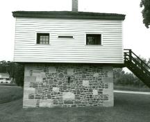 Side elevation of the Blockhouse, showing the ground floor of stone masonry and the timber framed upper storey covered with clapboard, 1989.; Department of Public Works / Ministère des Travaux publics, 1989.