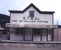 General view of the KTM Building, showing the painted, decorative, two-and-a-half-bay-retail façade with large retail windows, double entrance door and single door to the side, and its irregular arrangement of large retail windows, 1987.; Agence Parcs Canada / Parks Canada Agency, 1987.