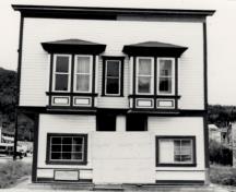 Vue de la façade générale de Ruby's Place, qui montre sa forme et son volume sur deux étages coiffés d’un toit à deux versants avec une fausse façade symétrique, 1987.; Parks Canada Agency / Agence Parcs Canada, 1987.