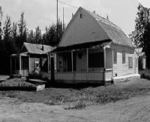 Vue en angle du chalet des invités, qui montre la forme caractéristique de son toit en comble brisé et la véranda à l’avant, 1988.; Parks Canada Agency / Agence Parcs Canada, 1988.