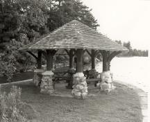 General view of the Gazebo, showing its octagonal, shingled roof, its rubble-stone piers, and its peeled-log posts and brackets, 1992.; Parks Canada Agency / Agence Parcs Canada / Historica Resources Ltd., 1992.
