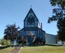 This image presents the steeply pitched roof and large rose window in the Gothic manner located above the front entrance, facing the St. Croix River.; PNB 2005