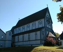 This image illustrates the exterior decorative detail including vertical board and batten panels and along the length of the church, a combination of double lancet windows below and round, star-shaped motif windows in the clerestory above.; PNB 2005